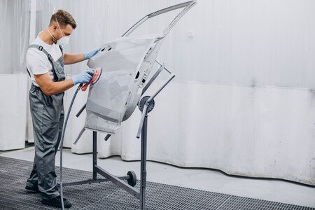 Auto body technician spray painting a vehicle door on a stand inside a paint booth